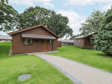 A pathway leading to wooden lodges surrounded by grass and trees at Luxury Lodge 69 in Dyserth