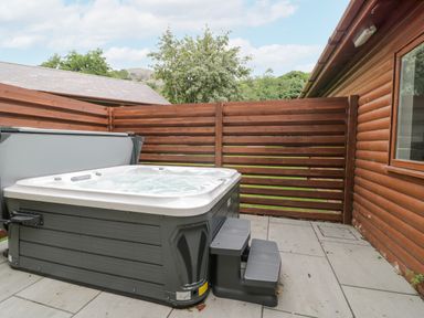 An outdoor hot tub with steps next to a wooden fence and log cabin wall at Luxury Lodge 69 in Dyserth
