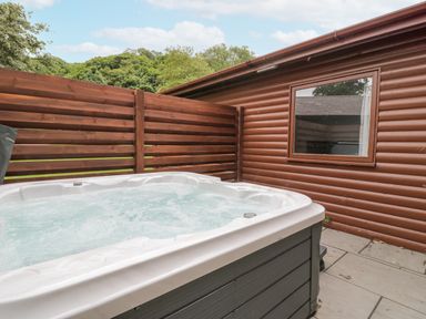 An outdoor hot tub next to a wooden fence and a log cabin wall with a window at Luxury Lodge 69 in Dyserth