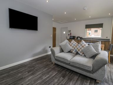 A living room with a sofa and cushions a wall mounted tv and a kitchen area at Luxury Lodge 69 in Dyserth