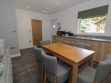 A dining area with a wooden table and six gray chairs next to a kitchen counter with a microwave toaster kettle and sink at Luxury Lodge 69 in Dyserth