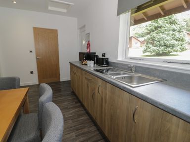 A kitchen with a wooden table and upholstered chairs beside wooden cabinets and a sink at Luxury Lodge 69 in Dyserth