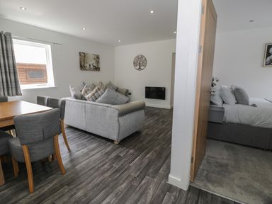 A living room with a dining table and chairs a sofa and wall decorations adjacent to a bedroom with a bed at Luxury Lodge 69 Dyserth