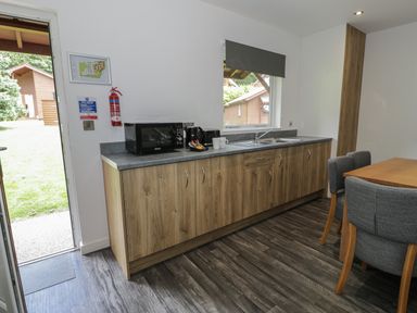 A kitchen area with wooden cabinets a microwave kettle toaster and a dining table with chairs at Luxury Lodge 69 in Dyserth