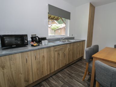 A kitchen with wooden cabinets a microwave kettle sink and a wooden dining table with gray chairs at Luxury Lodge 69 in Dyserth
