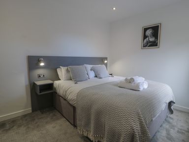 A bedroom with a double bed with pillows and towels on the bed a wall lamp and a framed artwork at Luxury Lodge 69 in Dyserth
