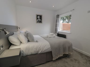 A bedroom with a double bed, bedside table, window with curtains and framed picture on wall at Luxury Lodge 69 in Dyserth