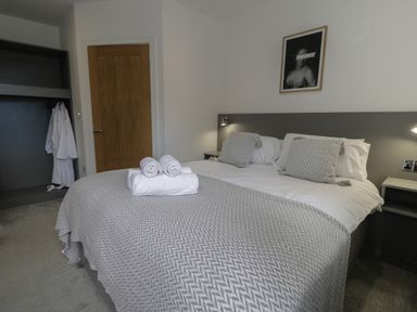 A bedroom with a double bed with pillows and towels and a wooden door and open wardrobe at Luxury Lodge 69 Dyserth