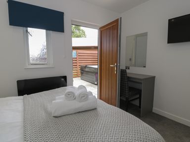 A bedroom with a bed and folded towels a desk with a chair a wall mounted TV and an open door leading outside at Luxury Lodge 69 in Dyserth