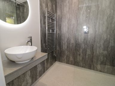 A bathroom with a round illuminated mirror a white vessel sink a chrome faucet and a heated towel rail at Luxury Lodge 69 in Dyserth
