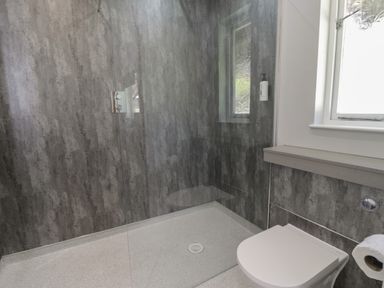 A bathroom with a walk-in shower a wall-mounted toilet and a window at Luxury Lodge 69 in Dyserth