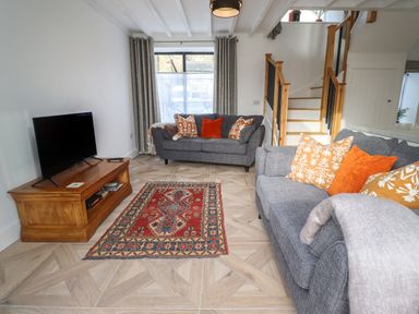 A living room with two grey sofas with orange and patterned cushions a wooden tv stand and a red patterned rug at Rowan Barn in Bellingham