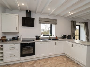 A kitchen with white cabinets a black oven and stove a window over a sink and grey curtains at Rowan Barn in Bellingham