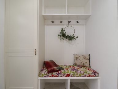 A white bench with a floral cushion a pillow and a blanket underneath hooks and shelves at Rowan Barn in Bellingham