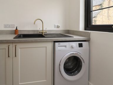 A kitchen counter with a sink washing machine and window at Rowan Barn in Bellingham