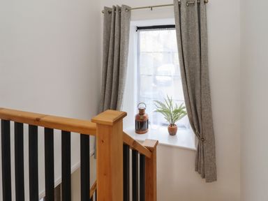 A window with closed curtains and a potted plant and lantern on the windowsill next to a wooden staircase railing at Rowan Barn in Bellingham