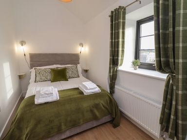 A bedroom with a double bed green blanket and pillows a window with green plaid curtains and a small plant on the sill at Rowan Barn in Bellingham