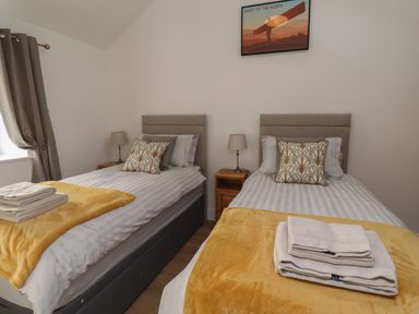 A bedroom with two single beds with yellow throws and patterned cushions at Rowan Barn in Bellingham