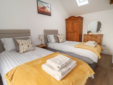 A bedroom with two single beds yellow blankets and folded towels a wooden wardrobe and dresser with mirror at Rowan Barn in Bellingham