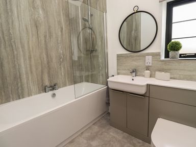 A bathroom with a bathtub shower combination a round mirror above a sink and a small plant on the windowsill at Rowan Barn in Bellingham