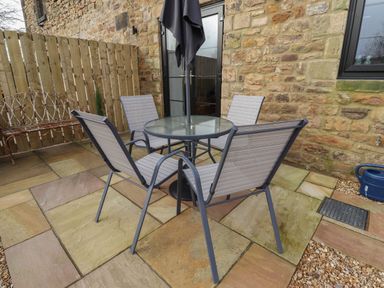An outdoor patio with a round glass table and four chairs next to a stone wall and wooden fence at Rowan Barn in Bellingham