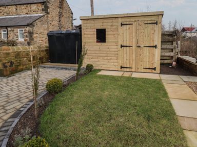 A garden with a wooden shed green grass stone paving and a stone wall at Rowan Barn in Bellingham