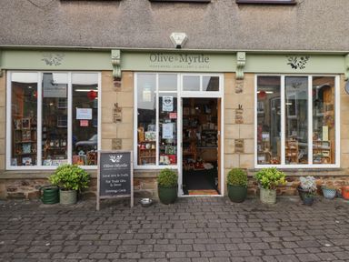 Front view of a shop named Olive and Myrtle with plants outside and a signboard on the pavement at Rowan Barn in Bellingham