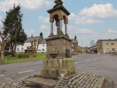 A stone monument with arches and columns on a cobblestone base in a village with houses and trees at Rowan Barn in Bellingham