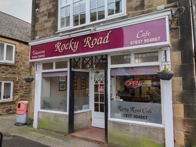 The exterior of Rocky Road Cafe with signage a neon open sign and hanging basket at Rowan Barn in Bellingham