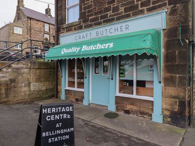 A craft butcher shop with a green awning and a heritage centre sign outside in a stone building in Bellingham