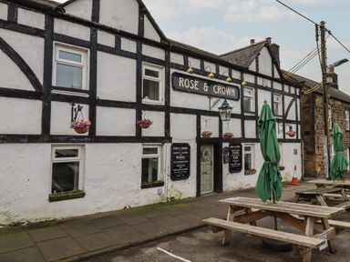 Exterior of a white building with black beams and a sign reading Rose and Crown with outdoor wooden picnic tables and green umbrellas folded Rowan Barn Bellingham