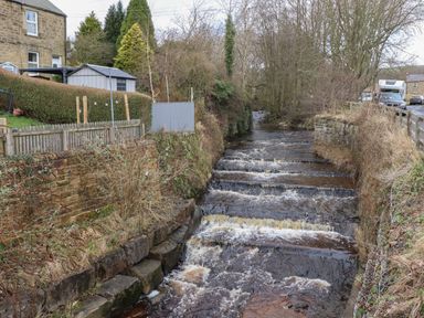 A small stepped river flowing between stone walls near houses and a road at Rowan Barn in Bellingham