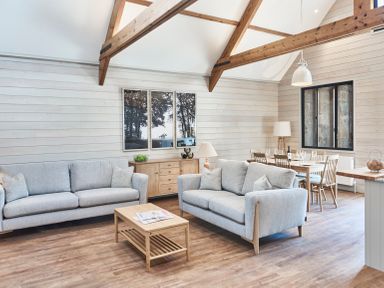 A living room with two sofas a coffee table and a dining table under wooden beams at The Hayloft in Humshaugh