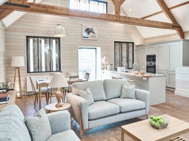 An open plan living room and kitchen with sofas, dining table, kitchen island, and wooden beams at The Hayloft in Humshaugh