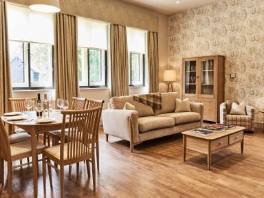 A living room with a dining table set with wine and plates and a sofa and armchair at The Stalls in Humshaugh
