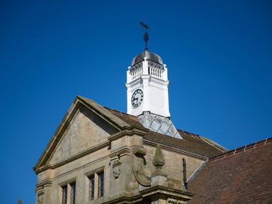 A clock tower on a stone building with a tiled roof and a weather vane against a clear blue sky at The Stalls in Humshaugh