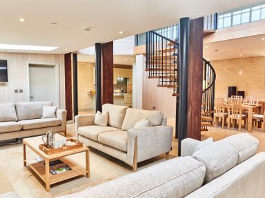 A living room with beige sofas a wooden coffee table a spiral staircase and a dining table at The Carriage House in Humshaugh