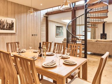 A dining area with a wooden table set with plates wine glasses and bottles near a spiral staircase and a living room at The Carriage House in Humshaugh