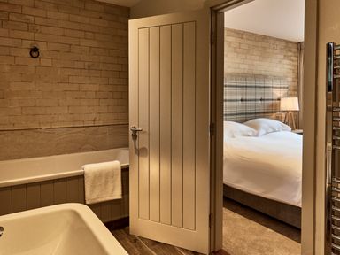 A bathroom with bathtub and towel next to a bedroom with a bed and bedside lamp at The Carriage House in Humshaugh