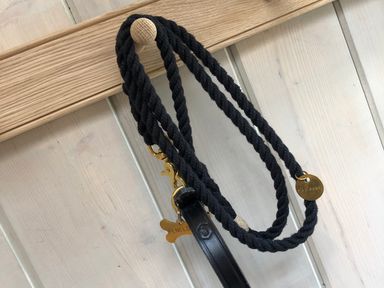 A black rope dog leash with gold tags hanging on a wooden peg on a light wood panel wall at The Carriage House in Humshaugh