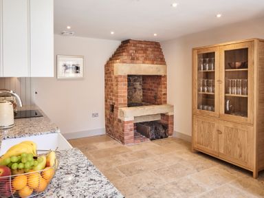 A kitchen with a brick fireplace a wooden cabinet with glass doors and a countertop with a fruit basket at The Smithy in Humshaugh