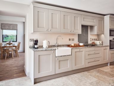 A kitchen with light-colored cabinets a granite countertop and a dining table visible in the background at The Smithy in Humshaugh