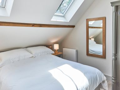 A bedroom with a bed a nightstand with a lamp a mirror and a skylight window at The Smithy in Humshaugh