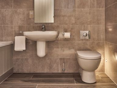 A bathroom with a wall-mounted sink a mirror a toilet and a towel at The Smithy in Humshaugh