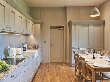 A kitchen with wooden floor gray cabinets a dining table set with plates wine glasses and a bottle at The Foal in Humshaugh
