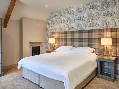 A bedroom with a bed with white bedding two bedside tables with lamps and a patterned wall at The Foal in Humshaugh