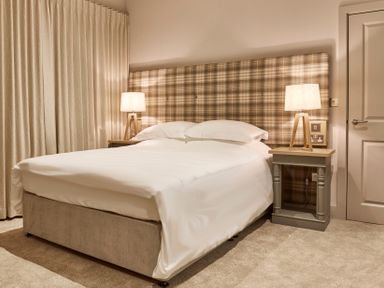 A bedroom with a bed with white bedding a plaid headboard two bedside tables with lamps and beige curtains at The Foal in Humshaugh