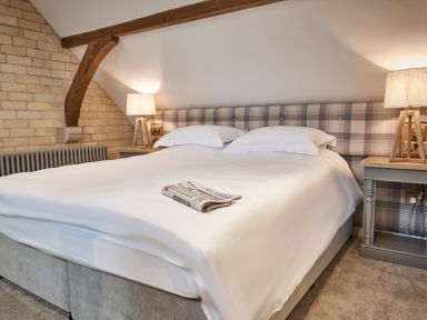 A bedroom with a bed covered in white linens and a newspaper on top two bedside tables with lamps and a wooden beam on the wall at The Foal in Humshaugh
