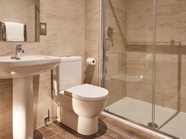 A bathroom with a pedestal sink a toilet a glass shower enclosure and tiled walls at The Foal in Humshaugh