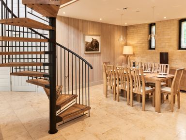 A dining room with a wooden table and chairs next to a spiral staircase at The Clocktower in Humshaugh